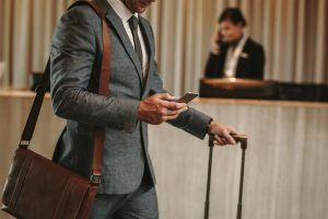 Man walking through hotel lobby with suitcase and looking at his phone