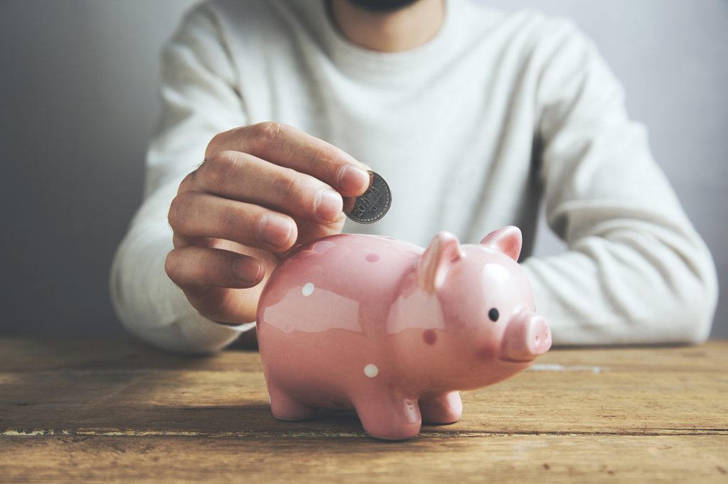 Savings: Man putting a coin into a piggy bank
