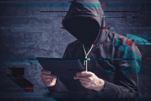 Ransomware criminal in hoodie looking at computer tablet.